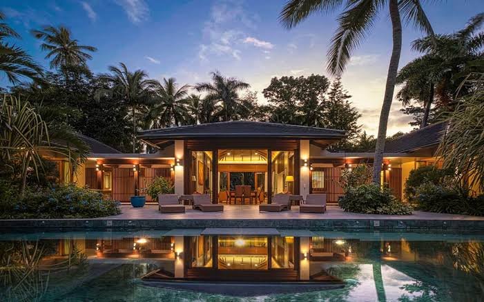 Tropical villa at dusk with warm interior glow and landscape lighting mirrored in the pool
