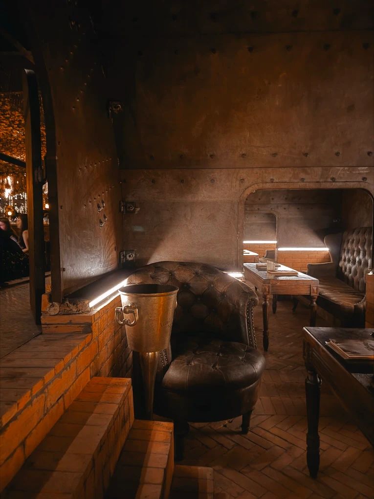 Warmly lit booth seating with brick detailing, leather chair, and rustic tables in an industrial lounge.